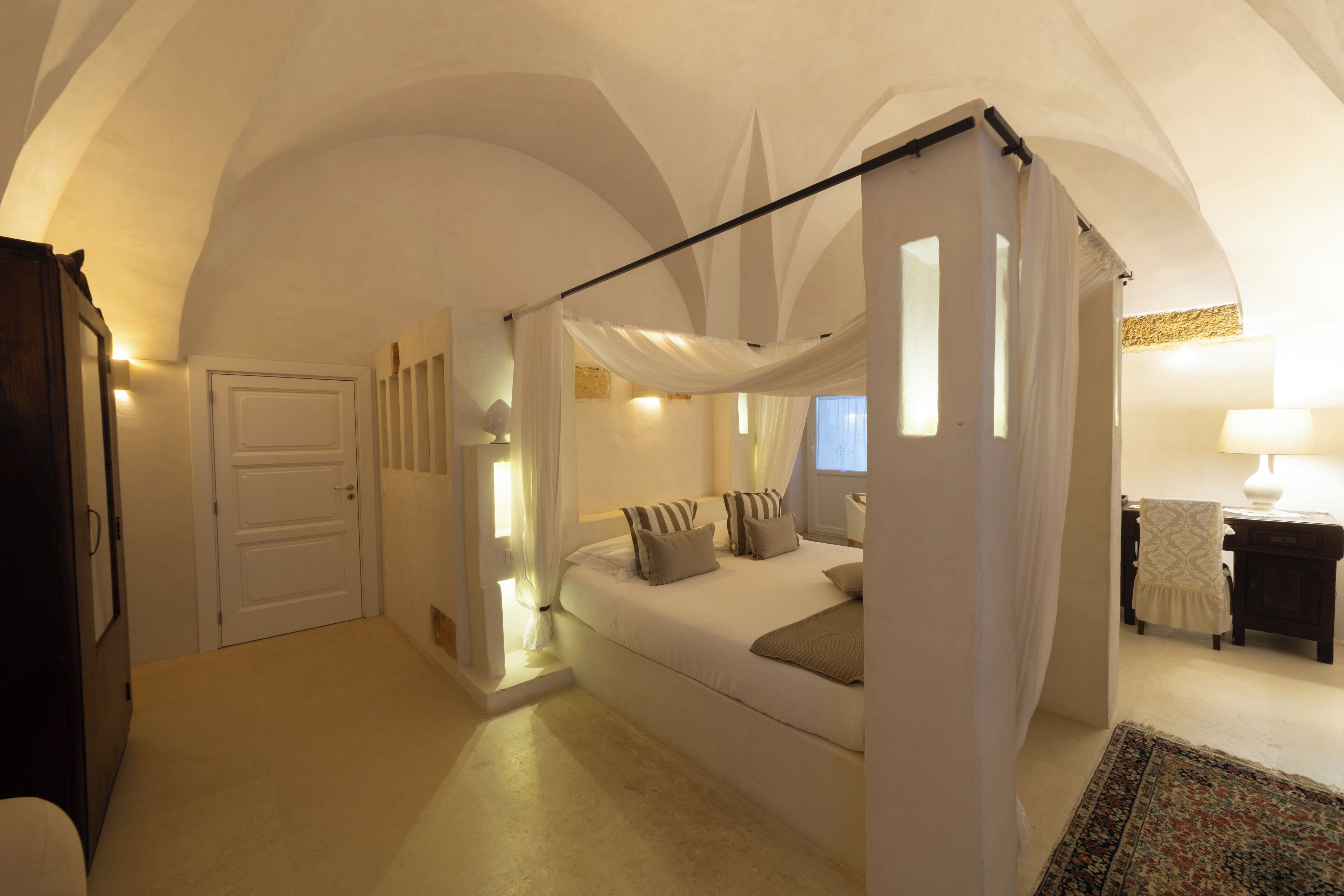 A bedroom with a canopy bed, a desk with a chair, and a lamp.