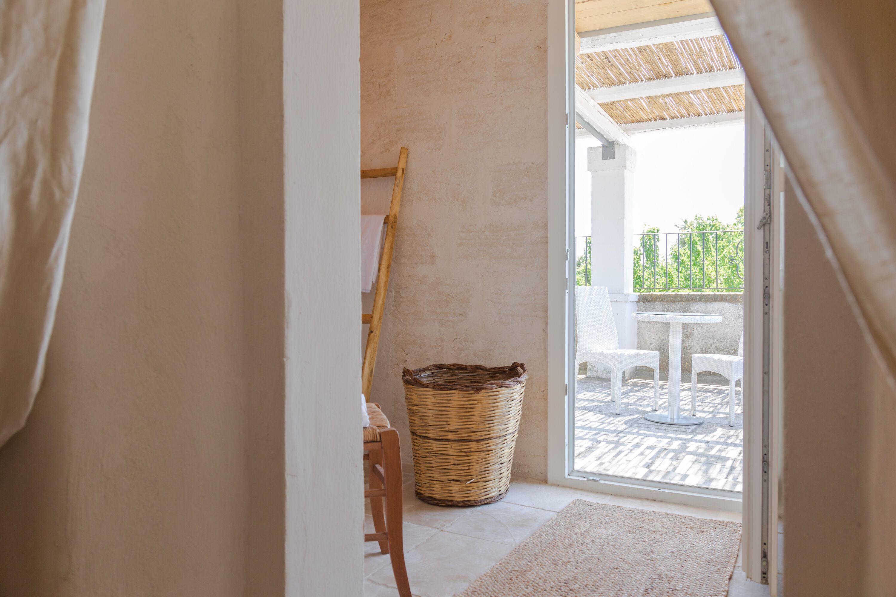 Una habitación con una cesta de mimbre, una silla de madera y vistas a un patio exterior con mesa y sillas.