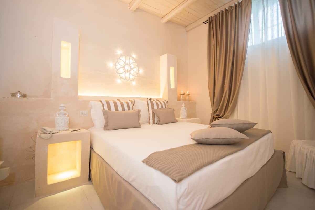 Une chambre d’hôtel avec un grand lit, des lampes de chevet, un luminaire décoratif fixé au mur et une vue sur l’extérieur à travers les rideaux.