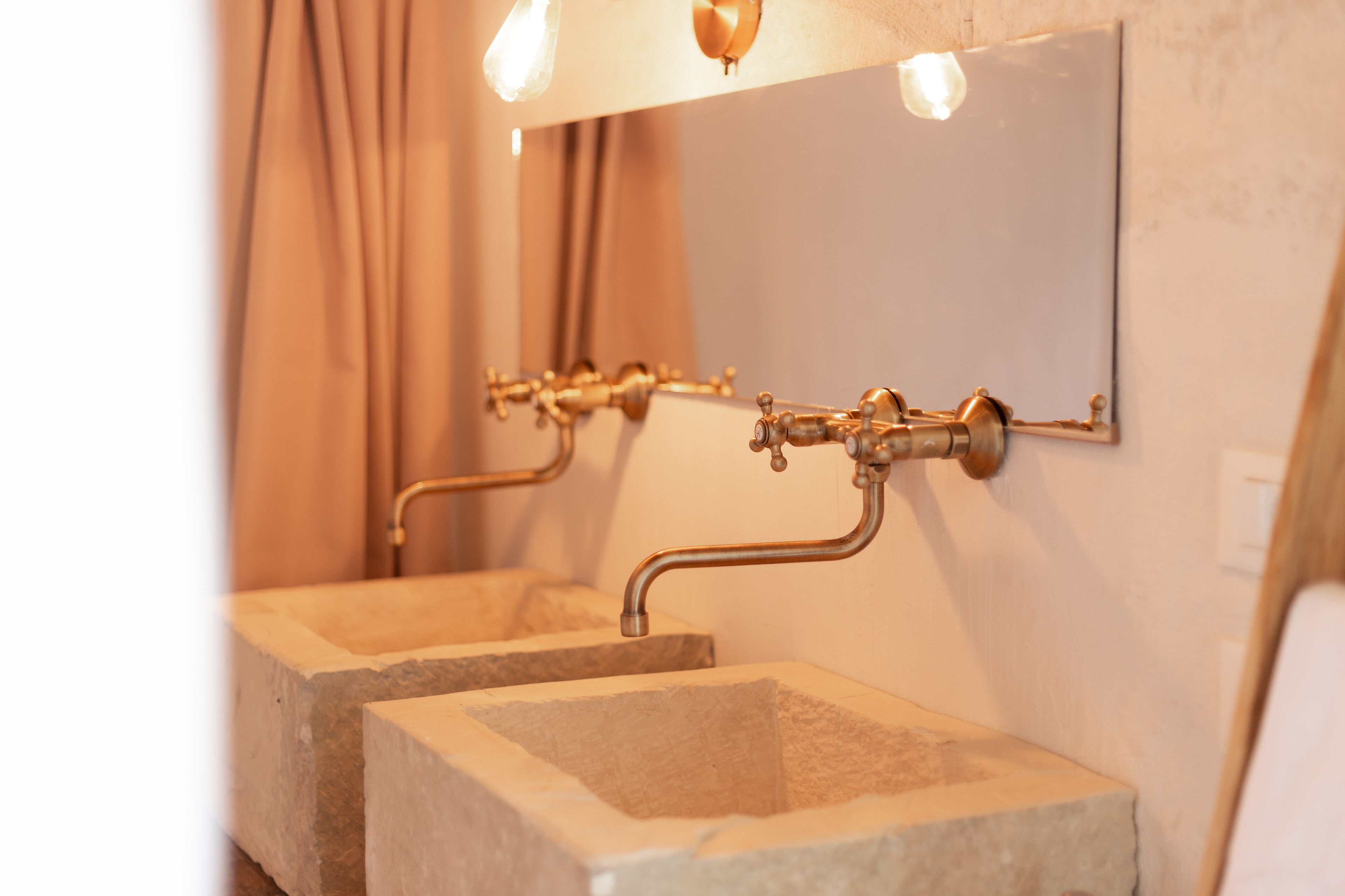 Ein Badezimmer mit zwei Steinwaschbecken, einem Spiegel und einem Wandarmaturen-Set.
