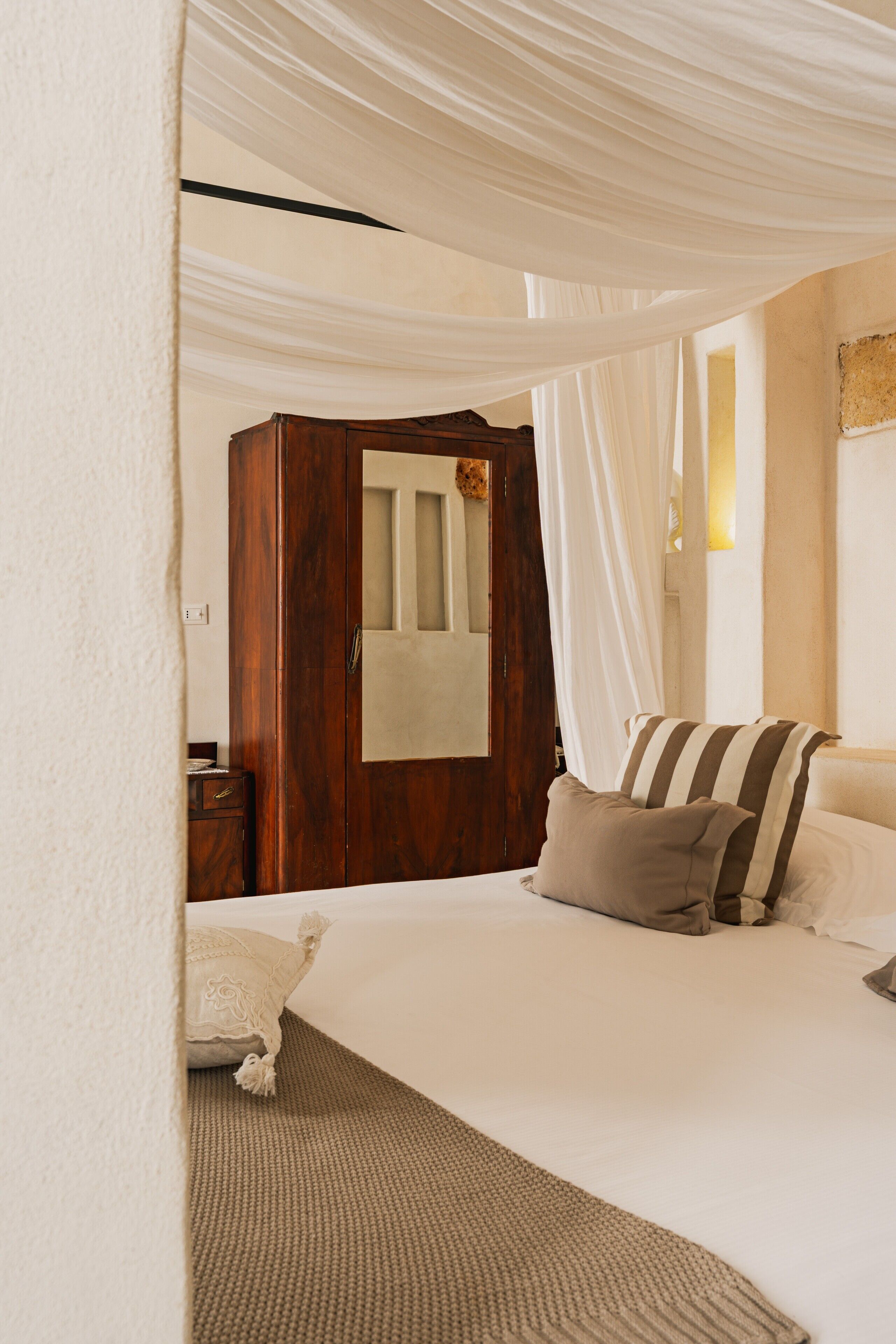 A bedroom with a large bed, a wooden wardrobe, and a white curtain.
