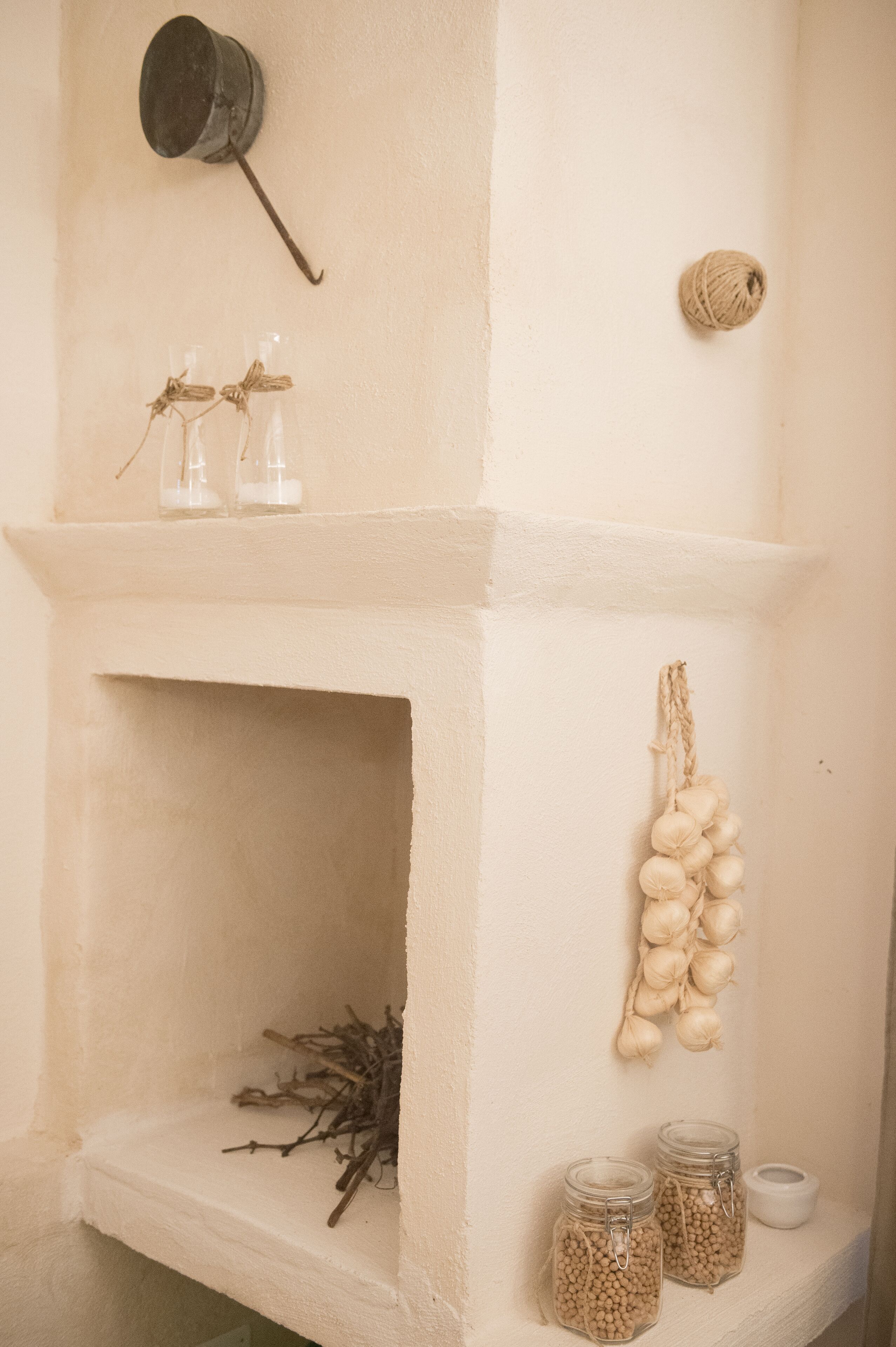 A white interior with a shelf holding jars, a hanging garlic bulb, and a rustic pot.