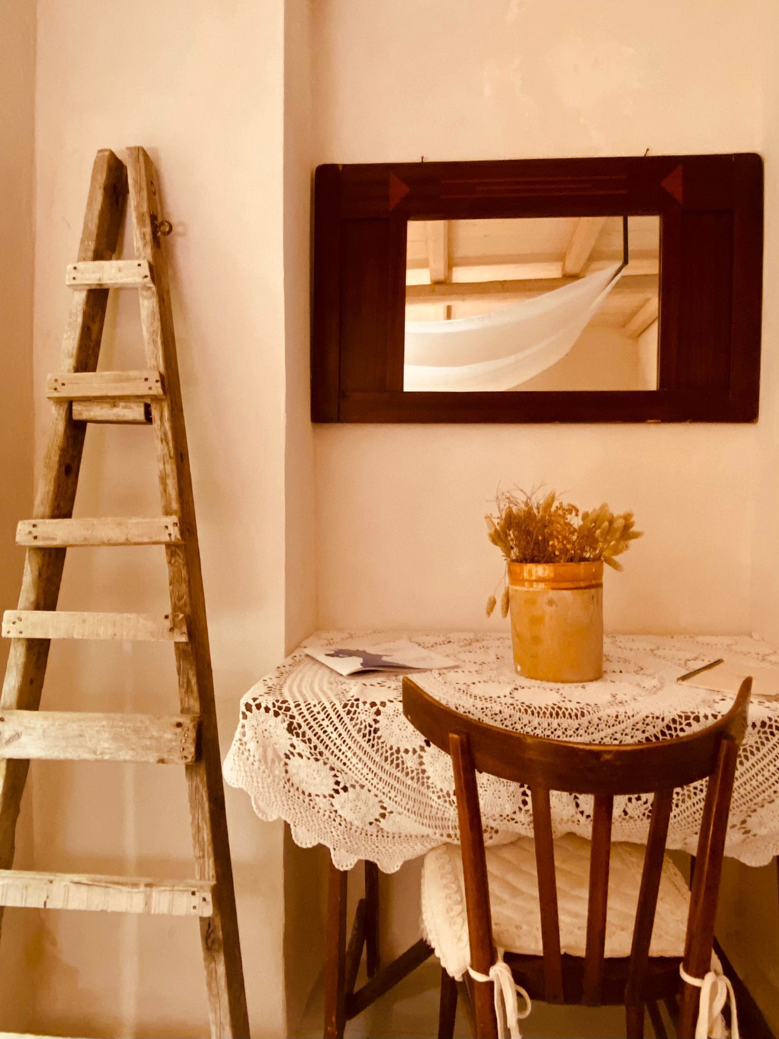A wooden ladder leaning against a wall, a small table with a lace tablecloth, a wooden chair, and a potted plant.