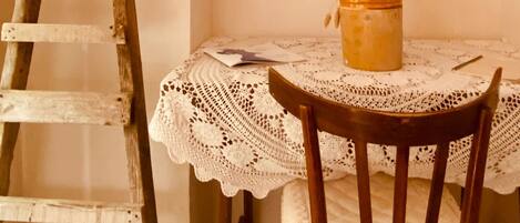 A wooden ladder leaning against a wall, a small table with a lace tablecloth, a wooden chair, and a potted plant.