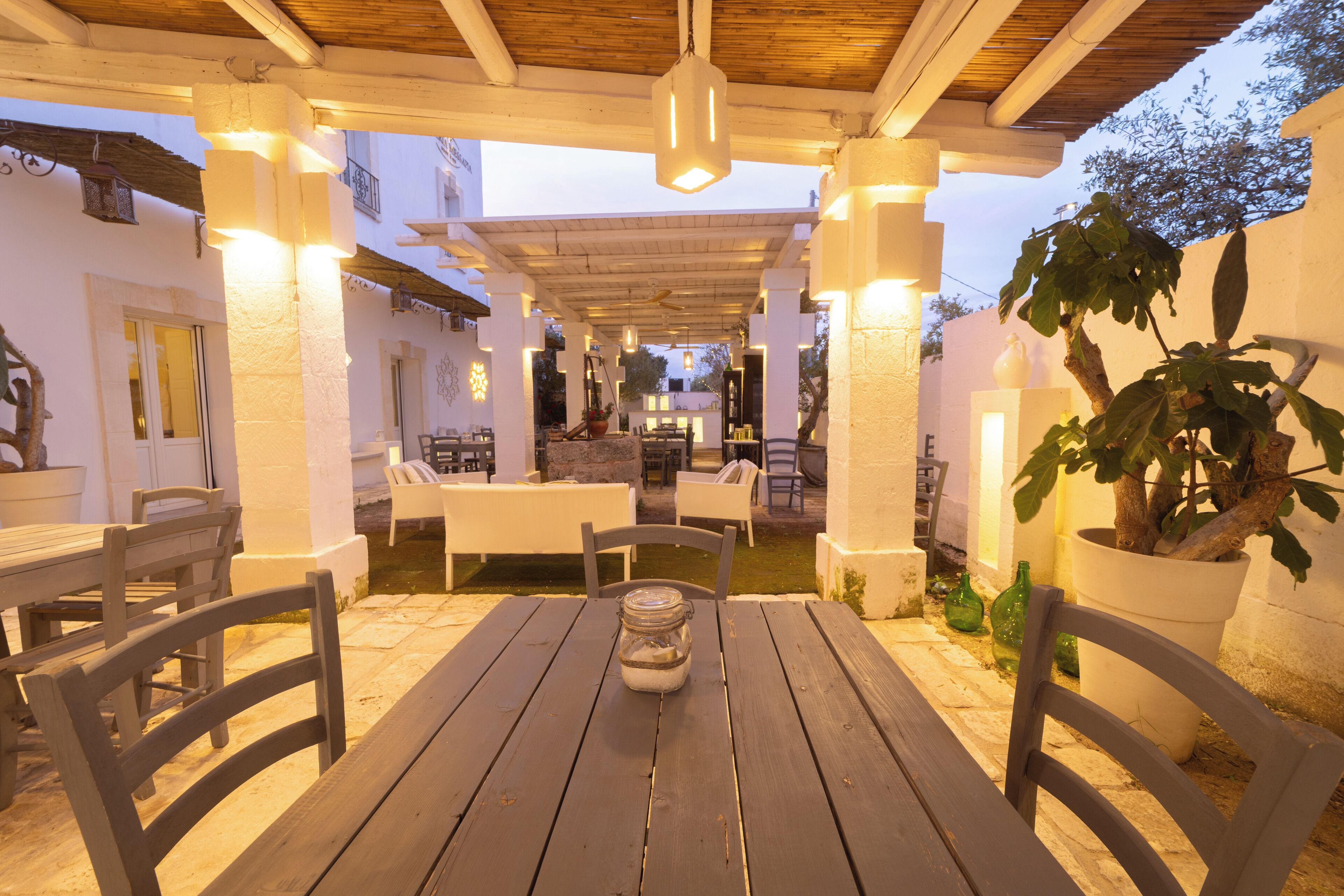 Un'area patio esterna con tavoli e sedie di legno, un lampadario e piante in vaso.