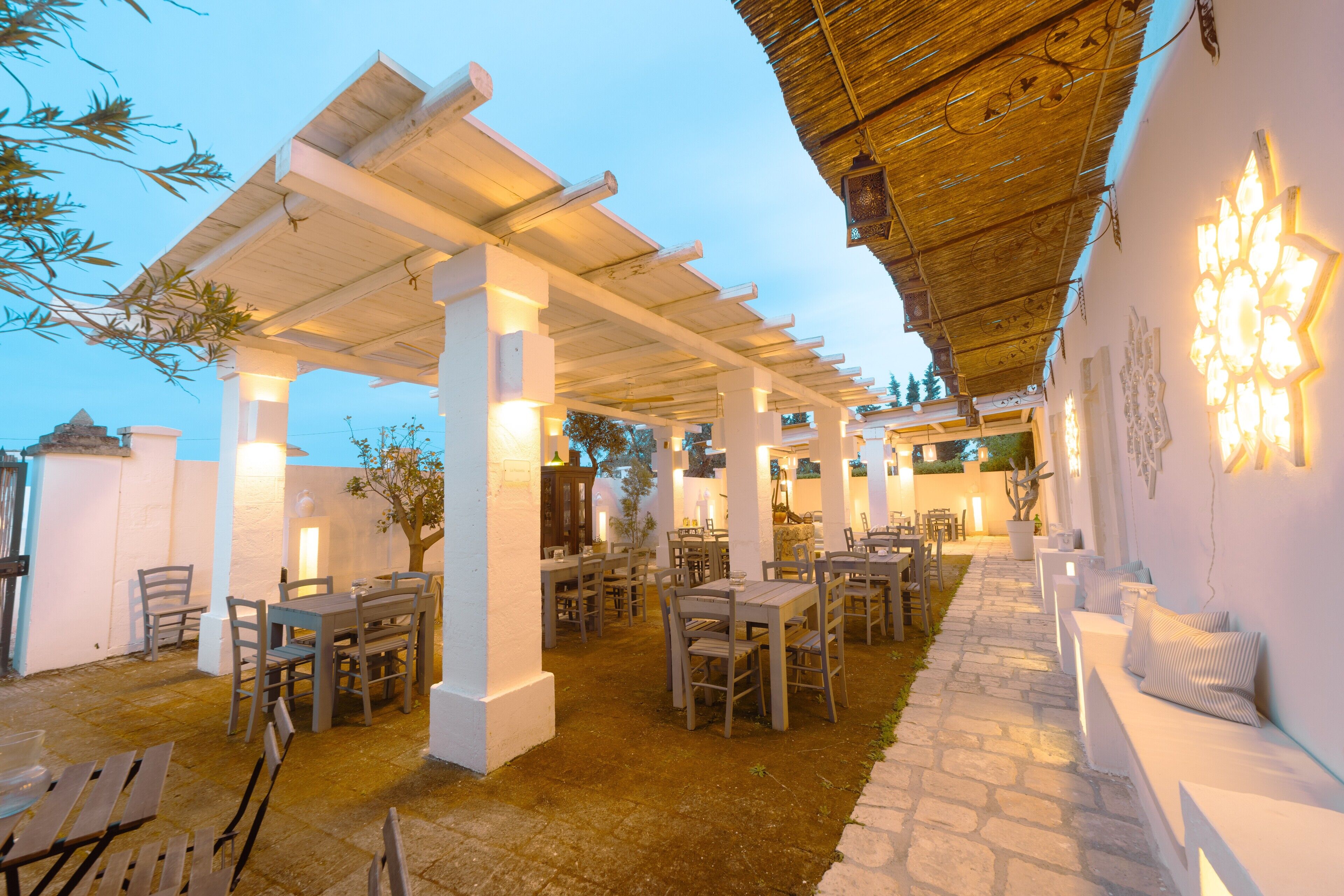 An outdoor patio area with tables and chairs, a stone pathway, and a thatched roof structure.
