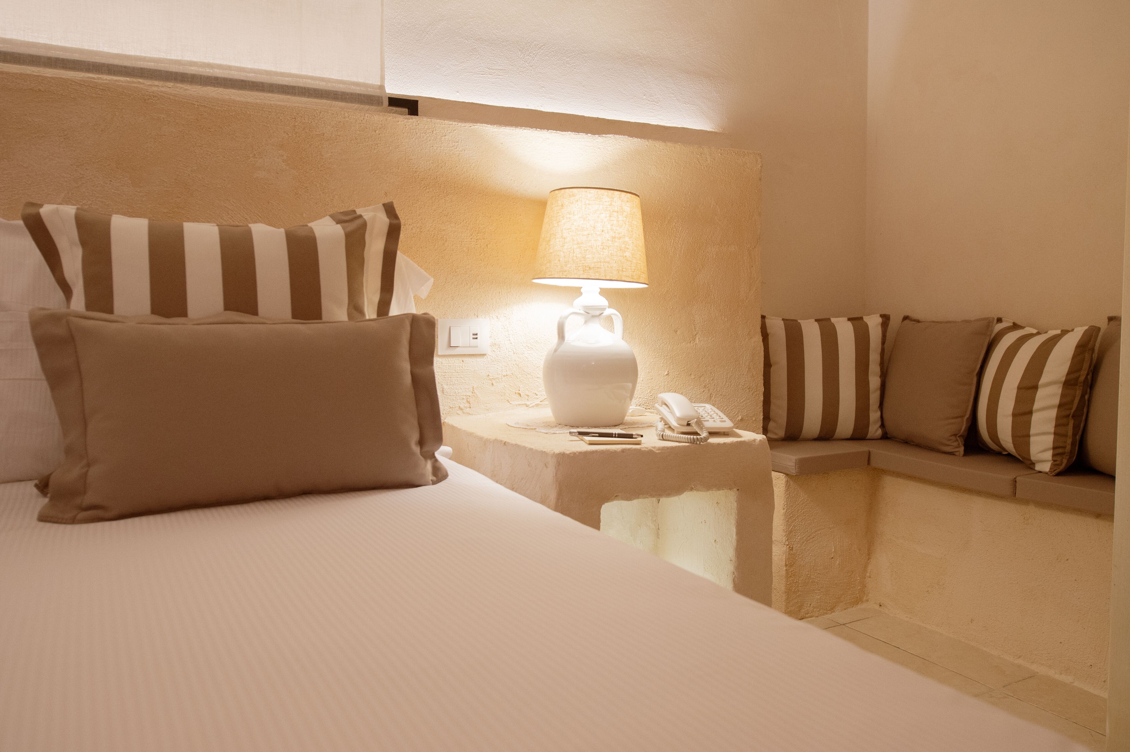Ein Hotelzimmer mit einem Bett, einer Nachttischlampe, einem Telefon und einem kleinen Tisch.