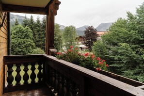 A wooden balcony with a view of a mountainous landscape and a building with red flowers in the foreground. - Hotel Schwarzer Adler (Tannheim)