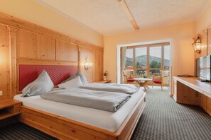 A hotel room with a bed, a desk, a chair, and a view of the mountains. - Hotel Schwarzer Adler (Tannheim)