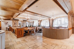 A spacious dining area with a high ceiling and exposed wooden beams, featuring a central island with seating and multiple chandeliers. - Hotel Schwarzer Adler (Tannheim)