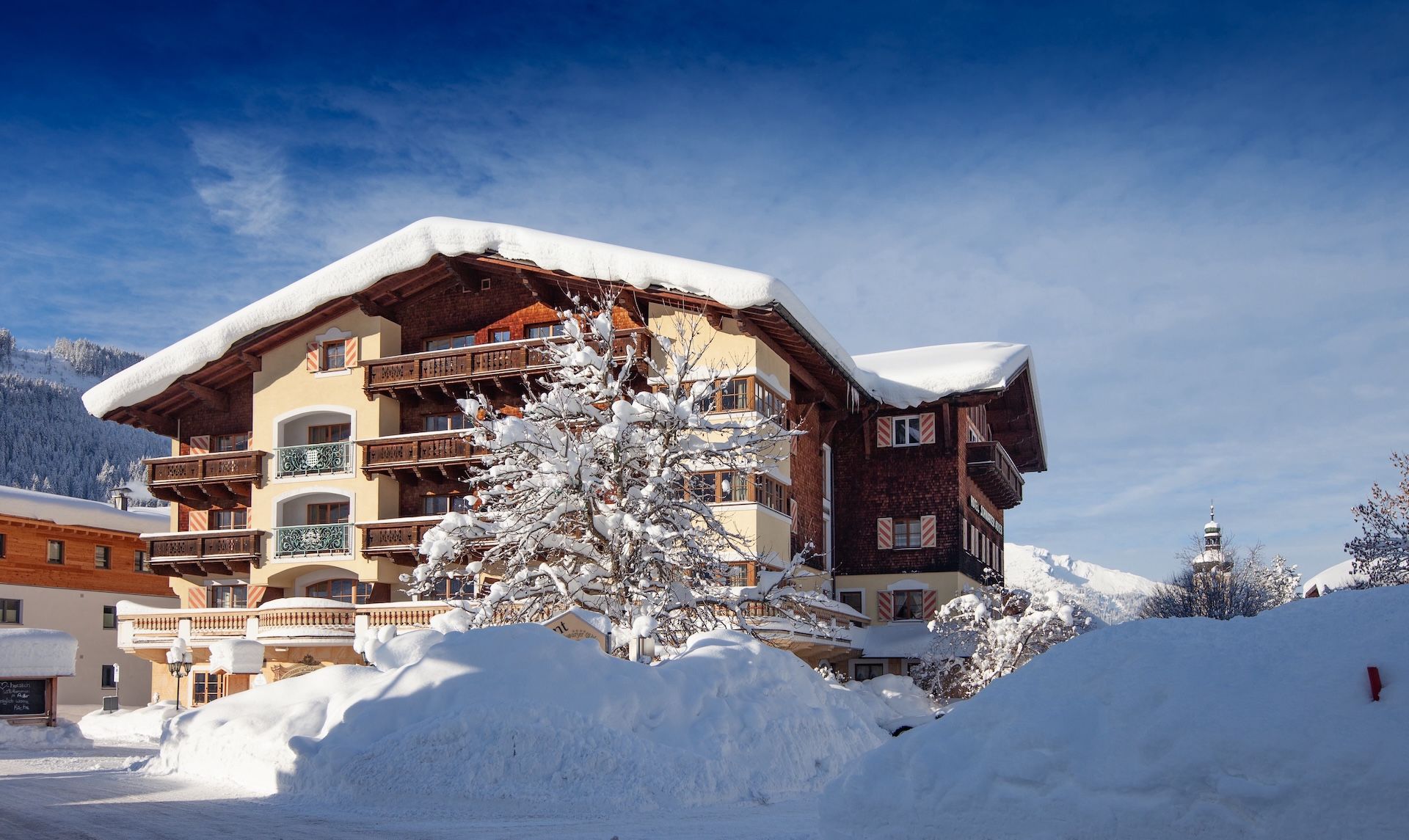 Un hôtel à plusieurs étages doté de balcons, entouré d’arbres couverts de neige et adossé à un paysage montagneux.