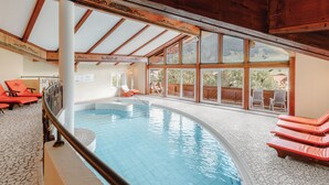 An indoor swimming pool with a view of a mountainous landscape through large windows. - Hotel Schwarzer Adler (Tannheim)