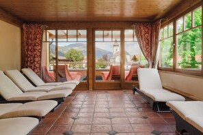 A room with a wooden ceiling, large windows, and a view of mountains and a church. - Hotel Schwarzer Adler (Tannheim)