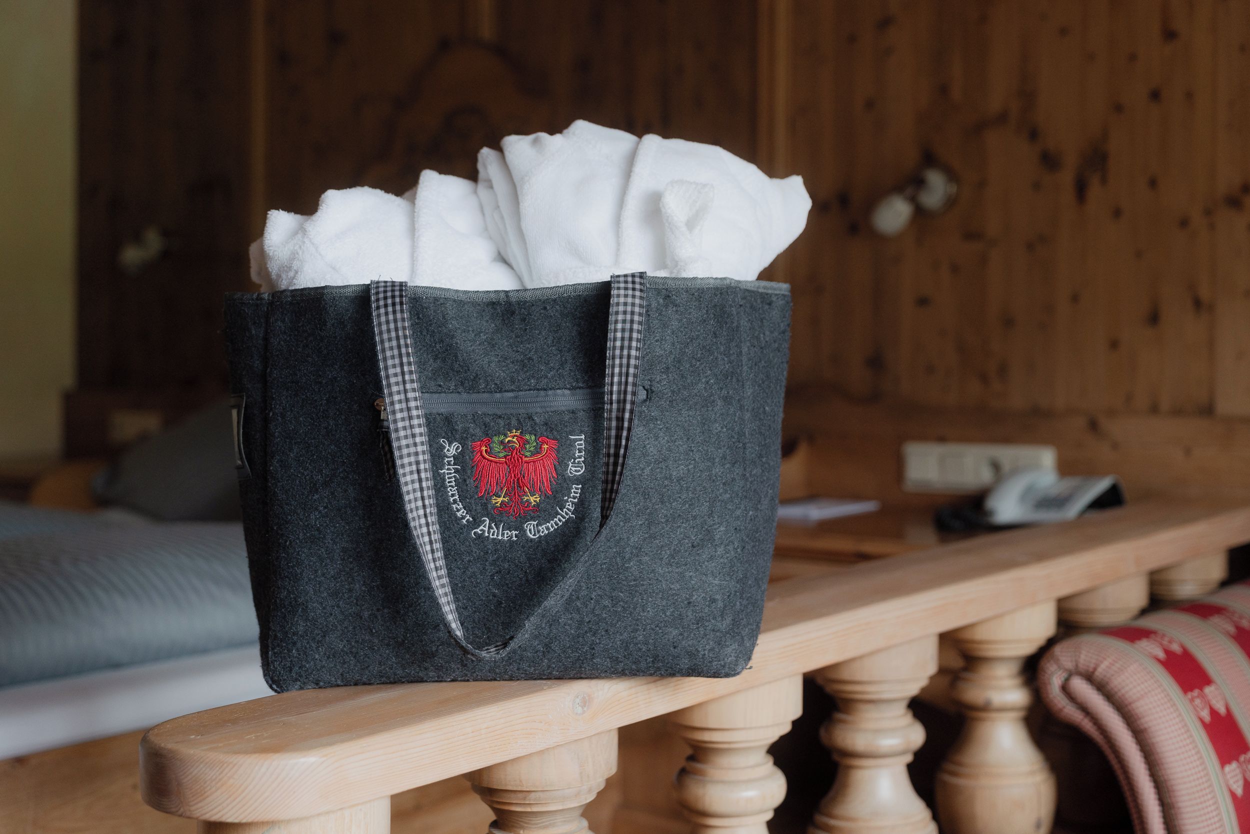 A dark grey tote bag with a checkered flap and embroidered text, placed on a wooden bench.