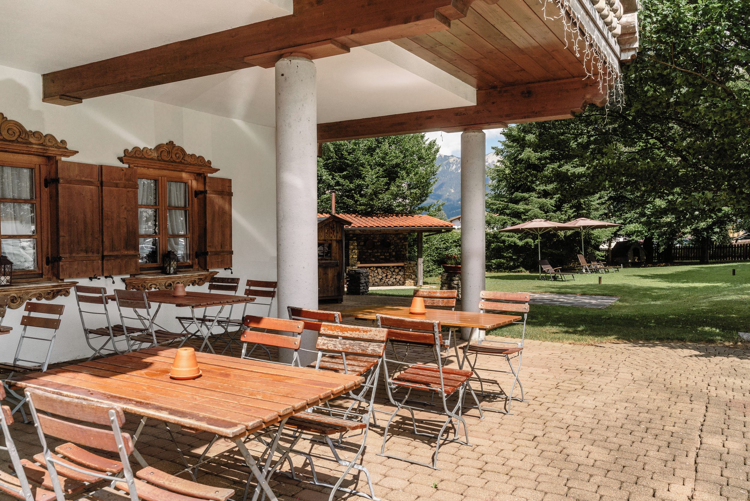 An outdoor patio with wooden tables and chairs, a stone wall, and a view of a mountain range.