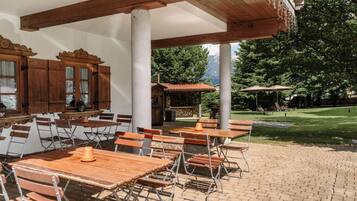 An outdoor patio with wooden tables and chairs, a stone wall, and a view of a mountain range.