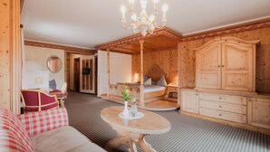 A cozy room with a wooden ceiling, a bed with a headboard, a wooden wardrobe, a round table with a vase, and a red and white checkered sofa. - Hotel Schwarzer Adler (Tannheim)