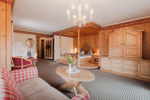Una habitación acogedora con techo de madera, una cama con cabecera, un armario de madera, una mesa redonda con un florero y un sofá a cuadros rojo y blanco.