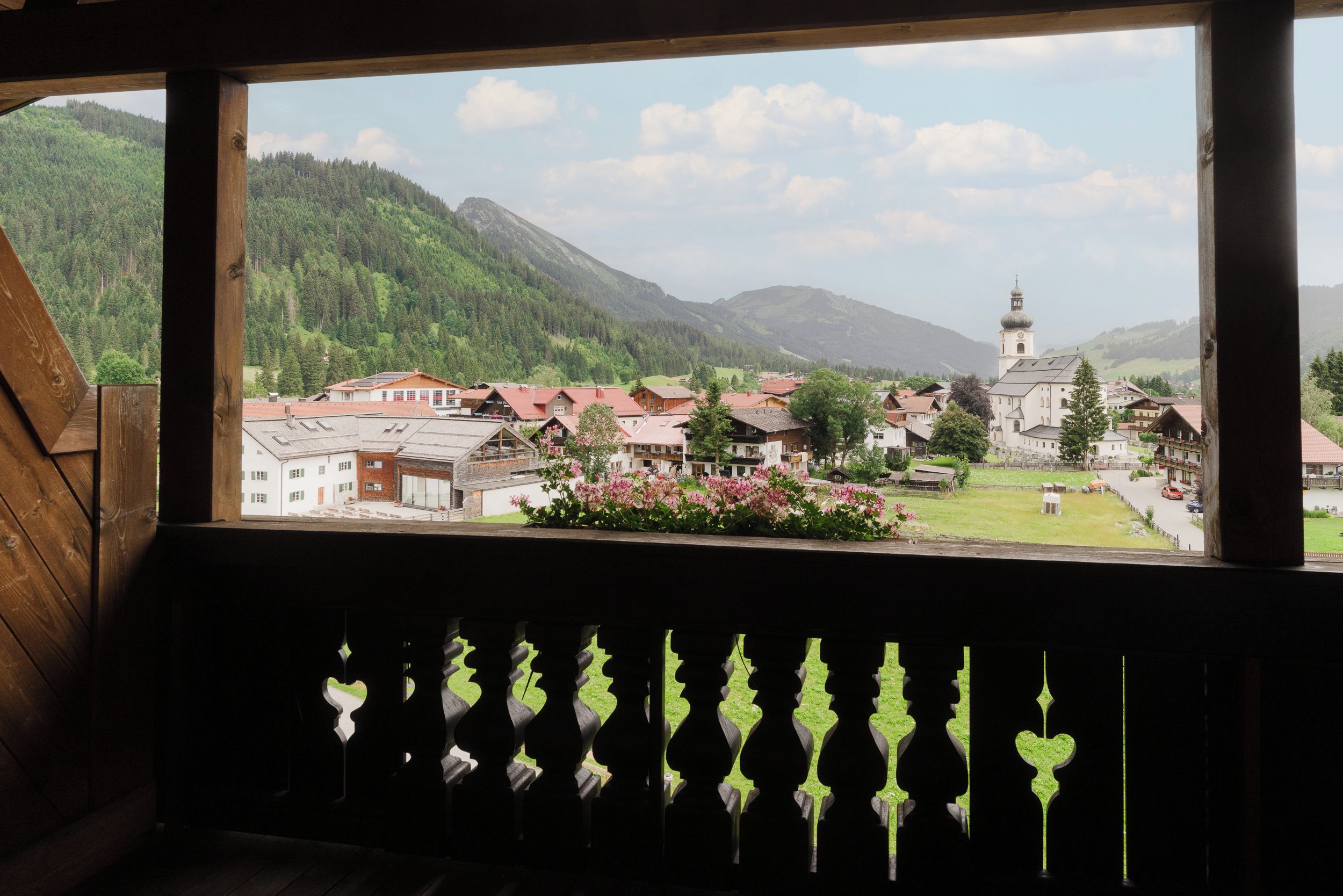 Vista da janela com vista para uma vila, uma igreja e montanhas ao fundo.