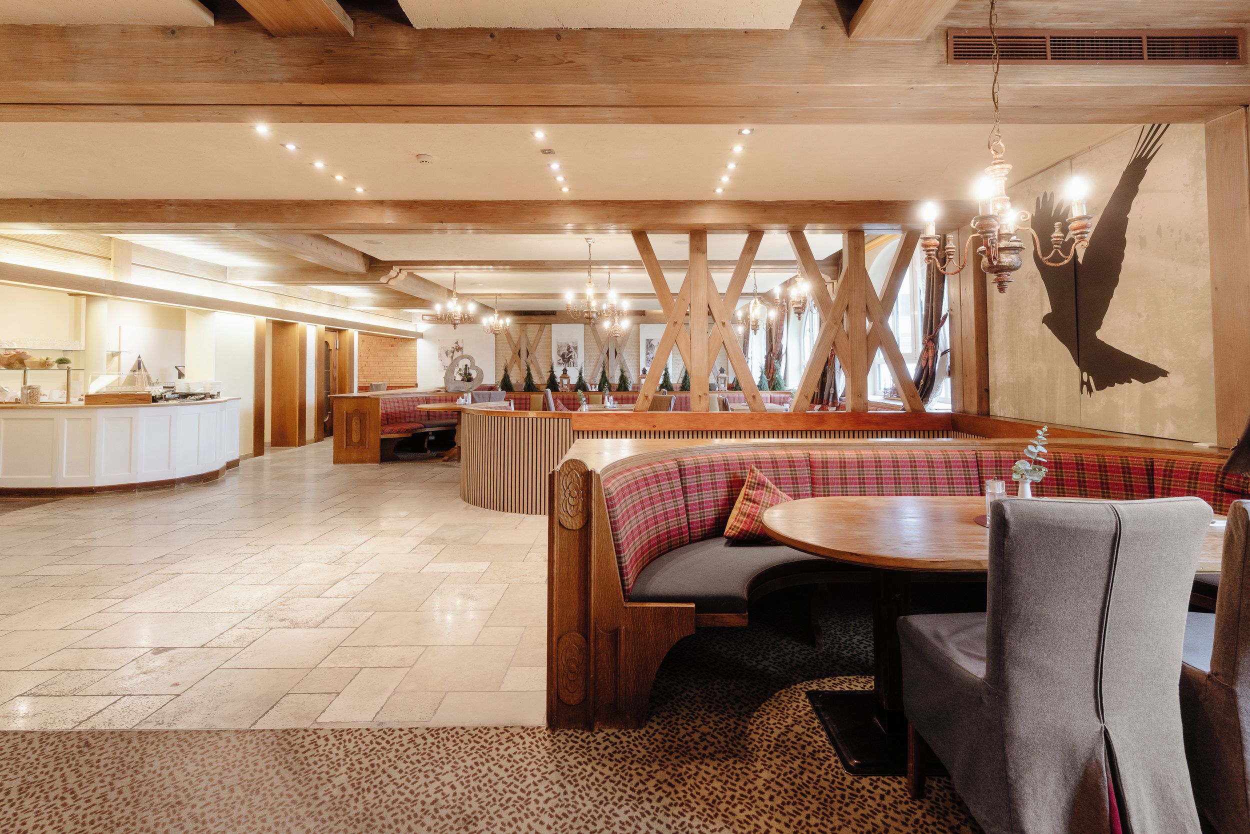Interior de restaurante com vigas de madeira, área de estar central com uma mesa redonda e um balcão com buffet.