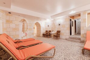 Una habitación con paredes de piedra, suelo de baldosas y un área de descanso con sillas y una mesa.