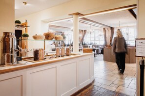 A cafe with a wooden counter, shelves with bowls and jars, and a menu board. - Hotel Schwarzer Adler (Tannheim)