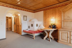 Una habitación de hotel con piso a cuadros, un banco de madera, una mesa con cafetera y una lámpara fijada a la pared.