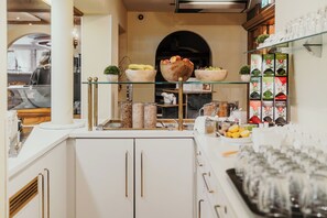 Una barra de desayuno con cuencos de fruta, una cafetera y una exhibición de productos envasados.