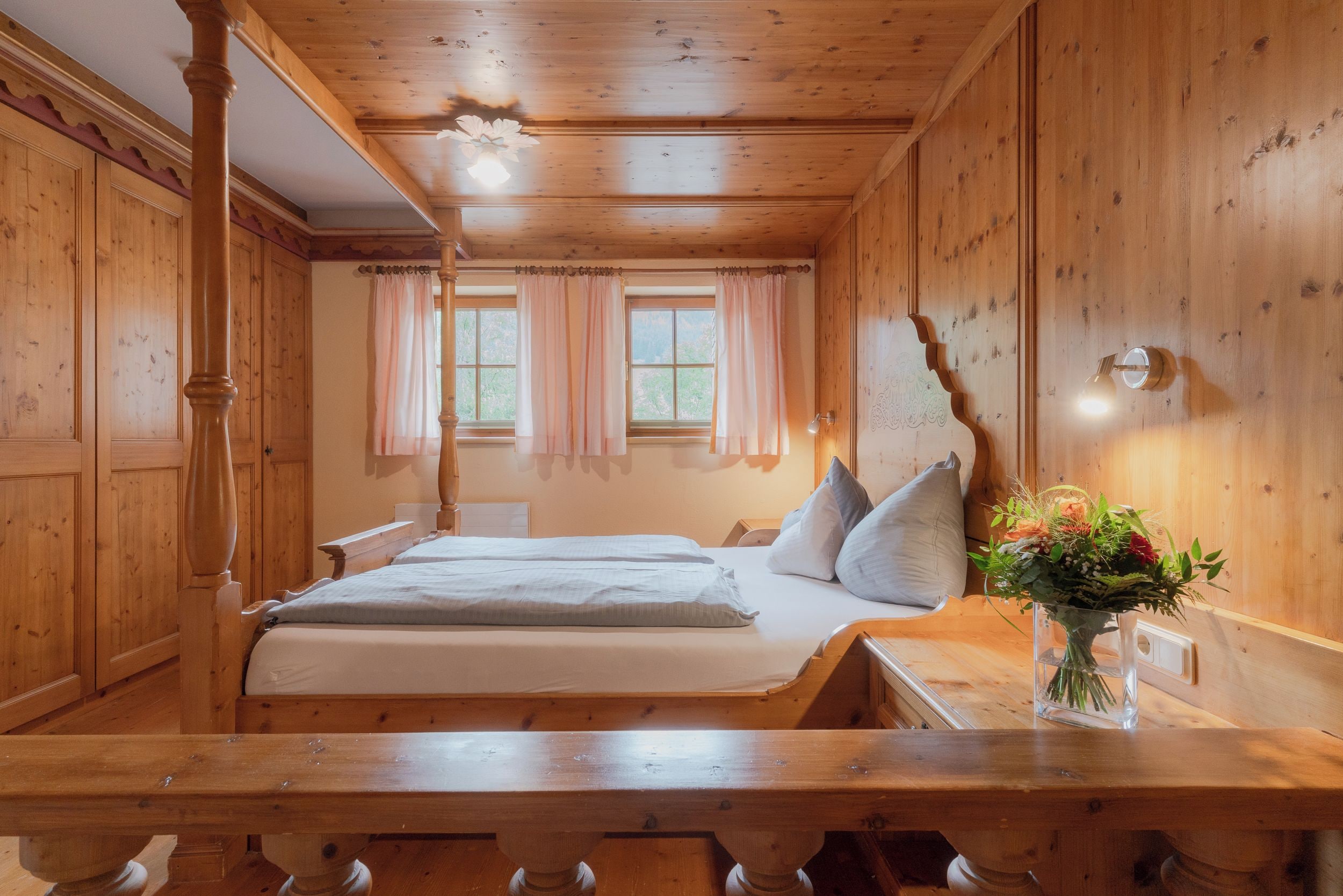 Una habitación de madera con una cama, una mesa y un florero con flores.