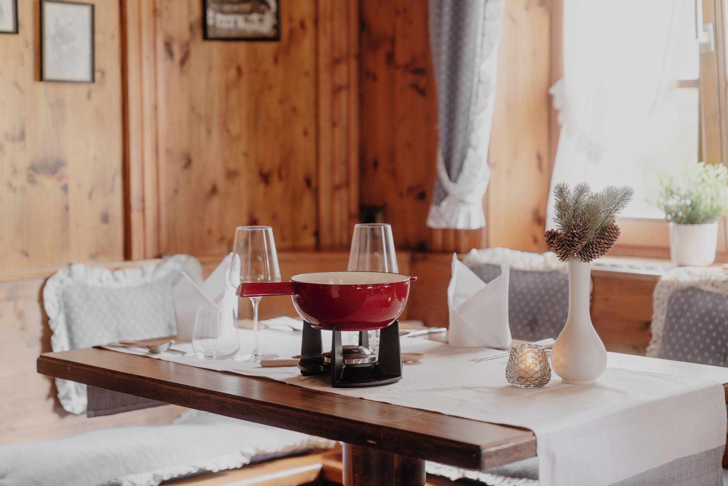 A dining table with a red pot, two glasses, and a candle.