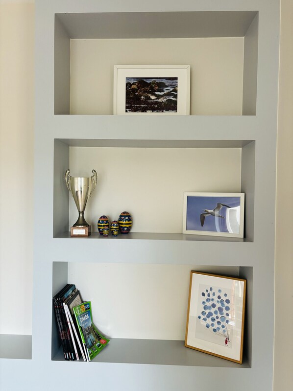 Una pared con tres estantes, cada uno mostrando diferentes objetos: una fotografía enmarcada, un trofeo, huevos decorativos, una imagen enmarcada de un pájaro y una obra de arte enmarcada.