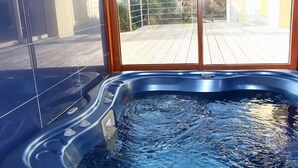 Ein Whirlpool mit Holzterrasse, Glasfenster und gefliesten Wänden.