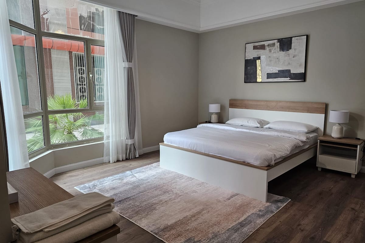 A modern bedroom with a large window, a bed, bedside tables, and a bench.