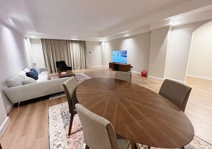 A modern living room with a round wooden table, a sofa, and a TV. - Al Faris Suite 2 (Manama)