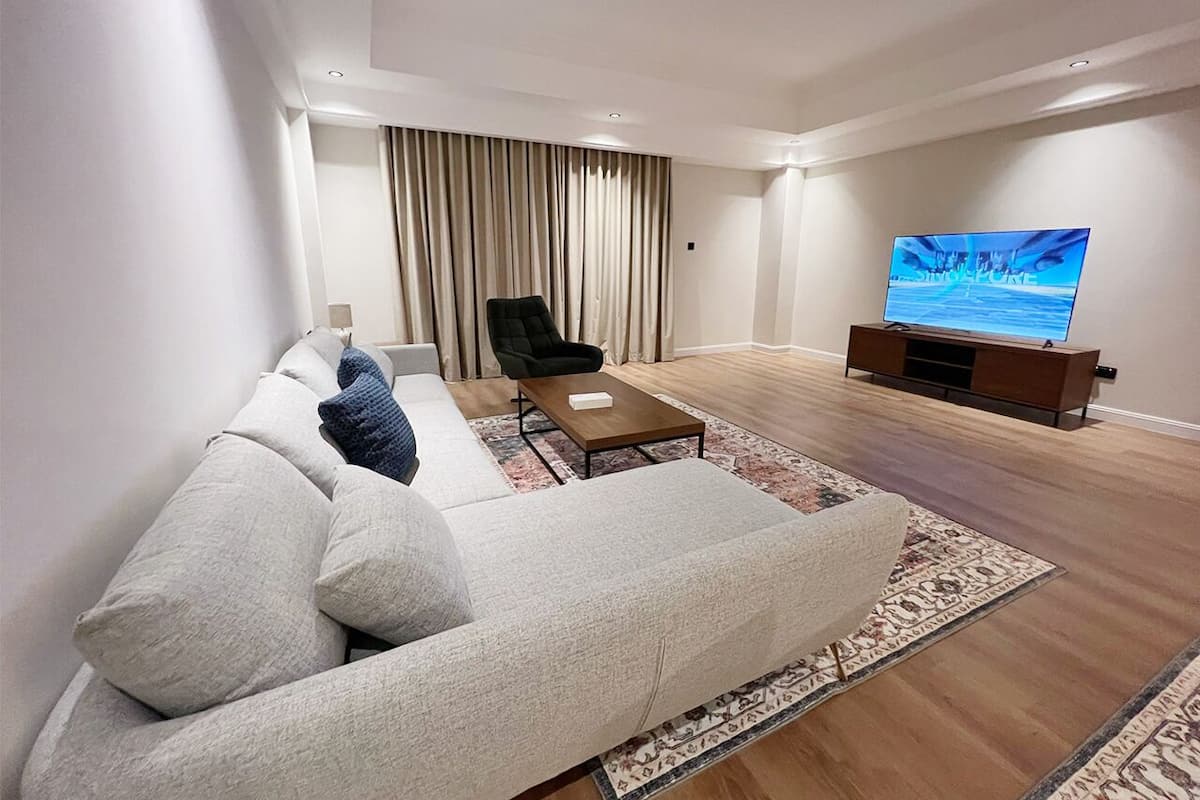 A modern living room with a sofa, a coffee table, a TV, and a large window with curtains.