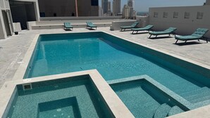 Piscina retangular com deck revestido e cadeiras de descanso ao redor.
