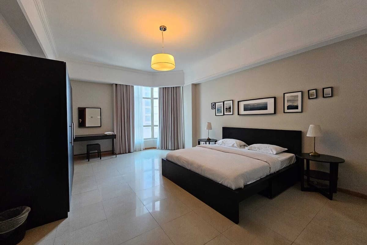 A modern hotel room with a large bed, a desk, and a view of the city through the window.