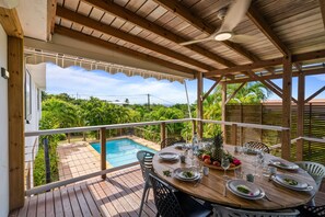 Une terrasse en bois avec une piscine, une table à manger pour quatre personnes et une vue sur une végétation luxuriante.