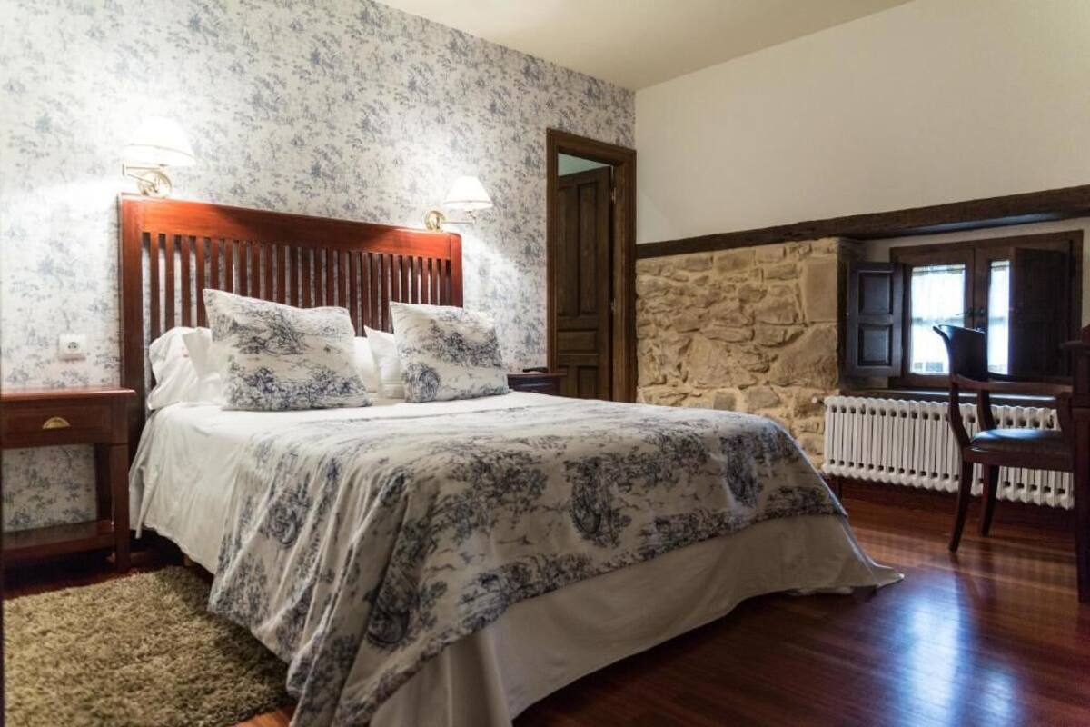 Une chambre à coucher avec un lit, deux lampes de chevet, un mur en pierre, un radiateur et une chaise.