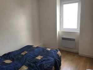 Une petite pièce, peu meublée, avec un lit simple, une fenêtre et un radiateur fixé au mur.