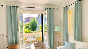Un salon comprenant un canapé, un fauteuil, une table et donnant sur une terrasse extérieure avec une table et des chaises.