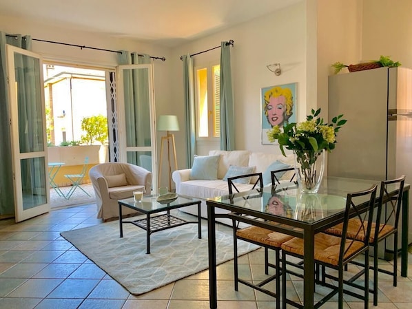 Un salon avec une table à manger en verre, un canapé et une table basse. Un tableau est accroché au mur et un vase rempli de fleurs est posé sur la table.