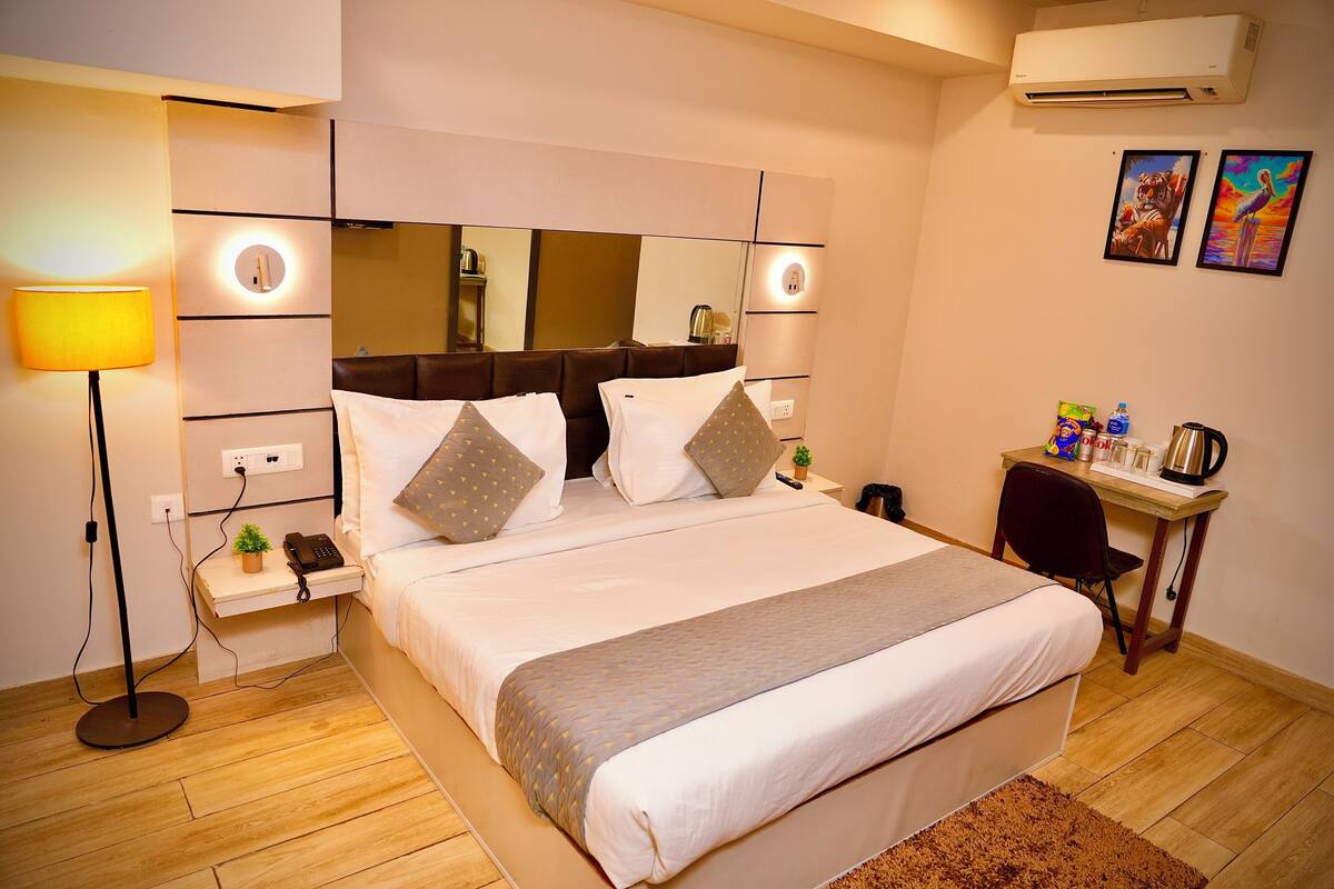 Habitación de hotel con cama, mesita de noche, lámpara, escritorio, silla y una obra de arte en la pared.