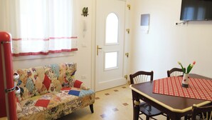 A room with a patterned sofa, a dining table with chairs, a TV mounted on the wall, and a door with a window.