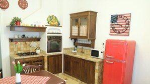 A compact kitchen with wooden cabinets, a red refrigerator, and a microwave. There is a clock with an American flag design on the wall.