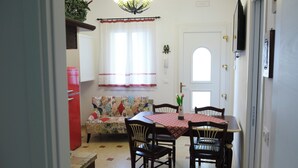 A dining area with a table set for four, a red refrigerator, a patterned sofa, and a window with curtains.