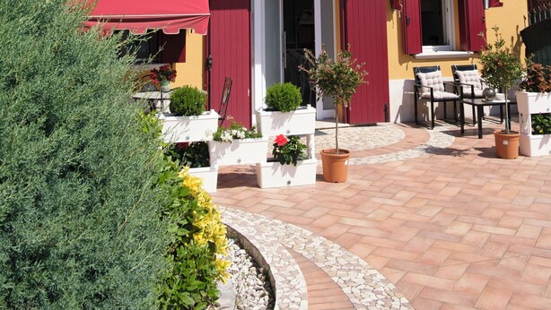 A two-story building with red awnings, a balcony, and a tiled patio area with outdoor furniture.