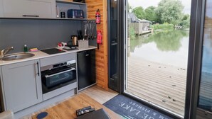 Eine kompakte Küche mit Spüle, Herd und Backofen, einem kleinen Kühlschrank und einem Fenster mit Blick auf ruhiges Wasser.
