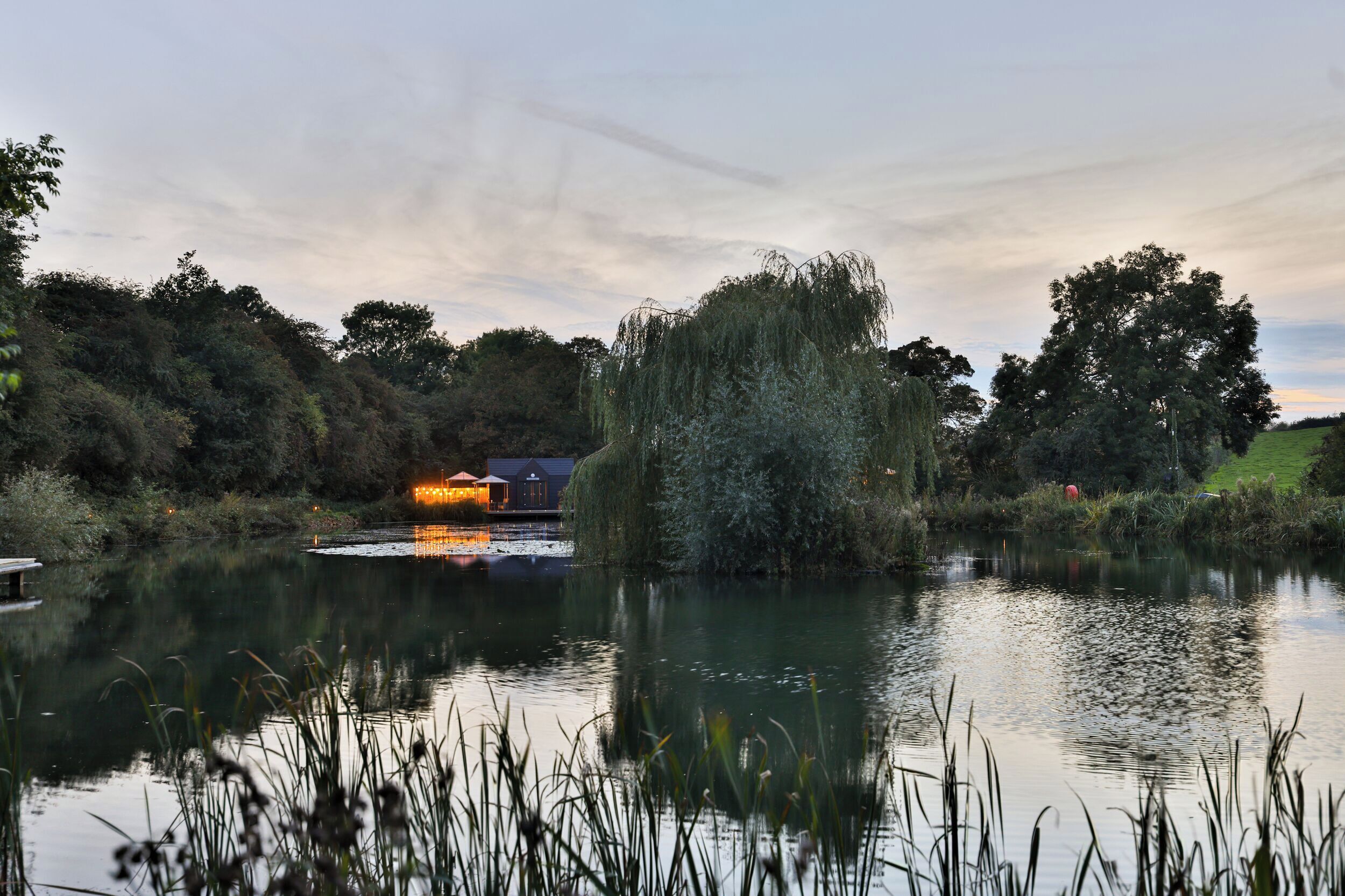 A serene lakeside setting with a small building reflecting on the water, surrounded by lush greenery and trees.