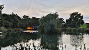 A serene lakeside setting with a small building reflecting on the water, surrounded by lush greenery and trees.